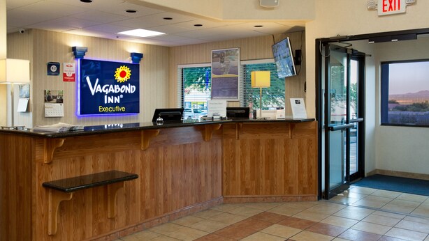 A reception desk with a sign for Vagabond Inn Executive, a clock, and an exit sign. - Vagabond Inn Executive - Green Valley (Green Valley)