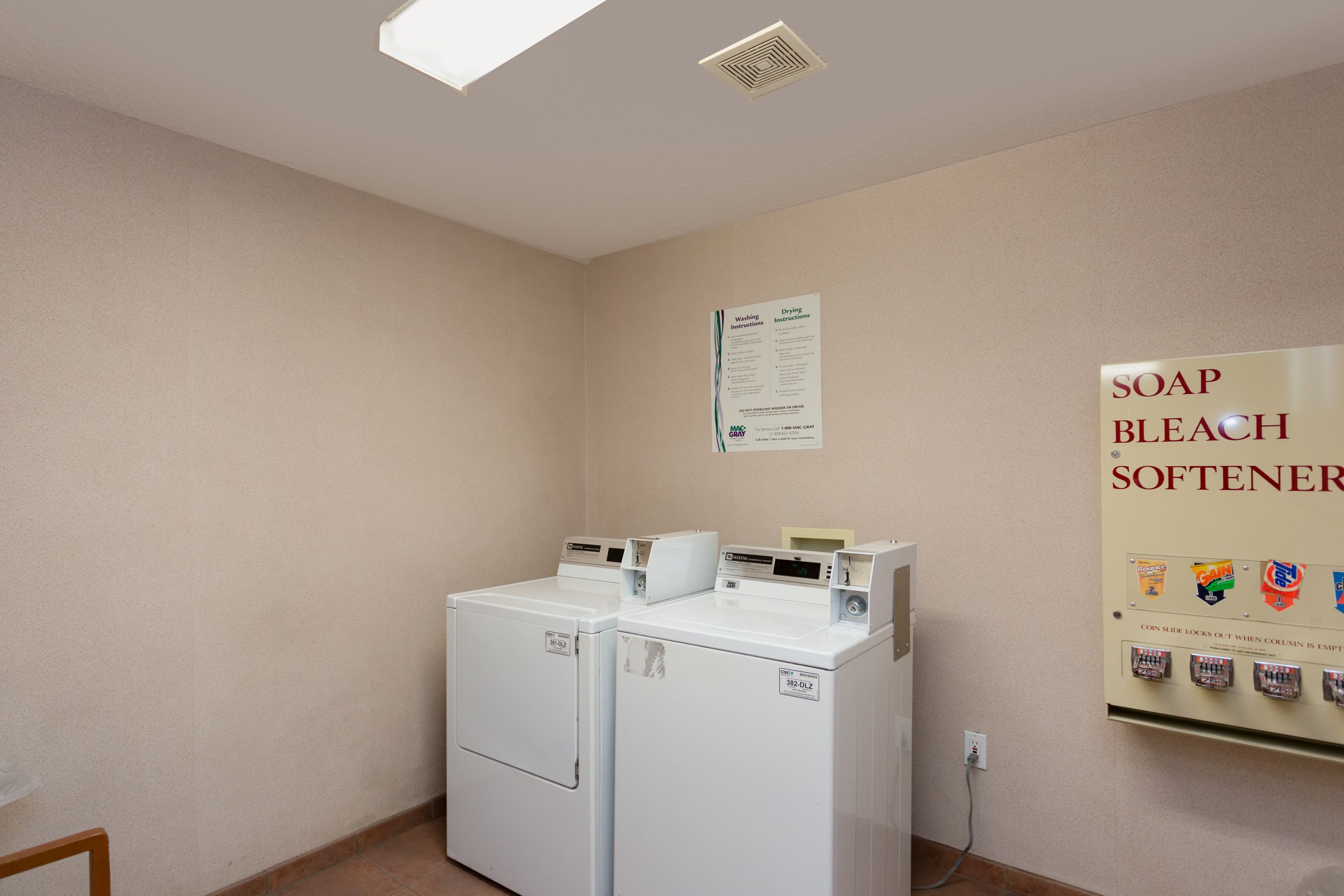 A laundry room with two white washers and dryers, a sign about soap and bleach softener, and a wall-mounted instruction poster.