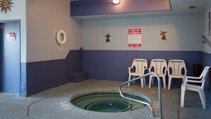 A small indoor pool with a diving board, white chairs, and a caution sign for spa users. - Vagabond Inn Executive - Green Valley (Green Valley)