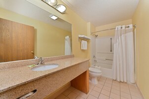 Un baño con lavamanos de encimera de granito, espejo, inodoro y ducha con cortina.