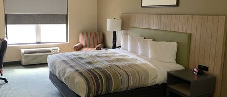 A hotel room with a large bed, a chair, a desk, and a window with blinds.