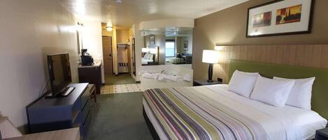 Habitación de hotel con cama, escritorio, silla, televisor, lámpara y baño a la vista.