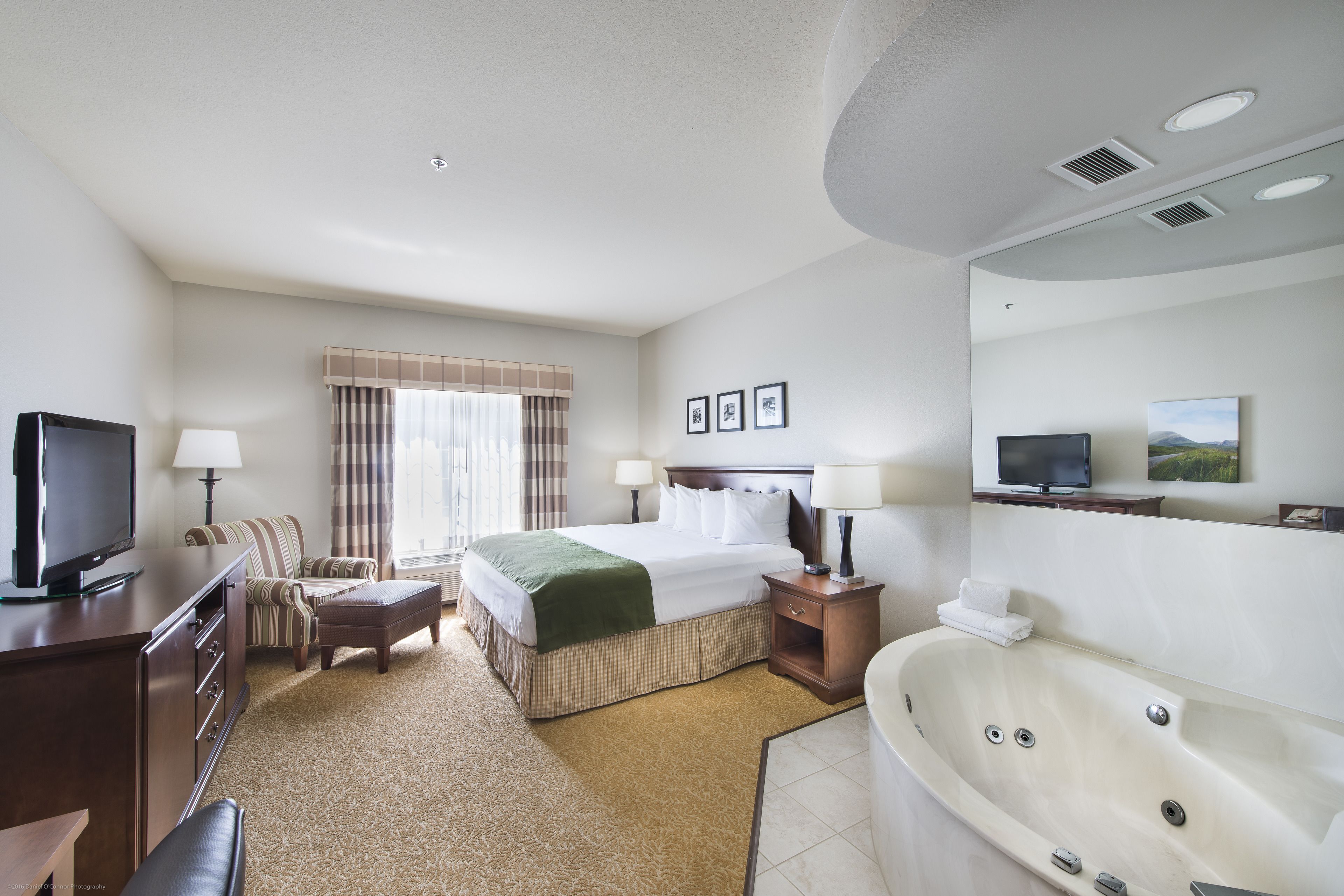 A hotel room with a bed, a television, a desk, a chair, a sofa, a bathroom with a bathtub, and a window with curtains.