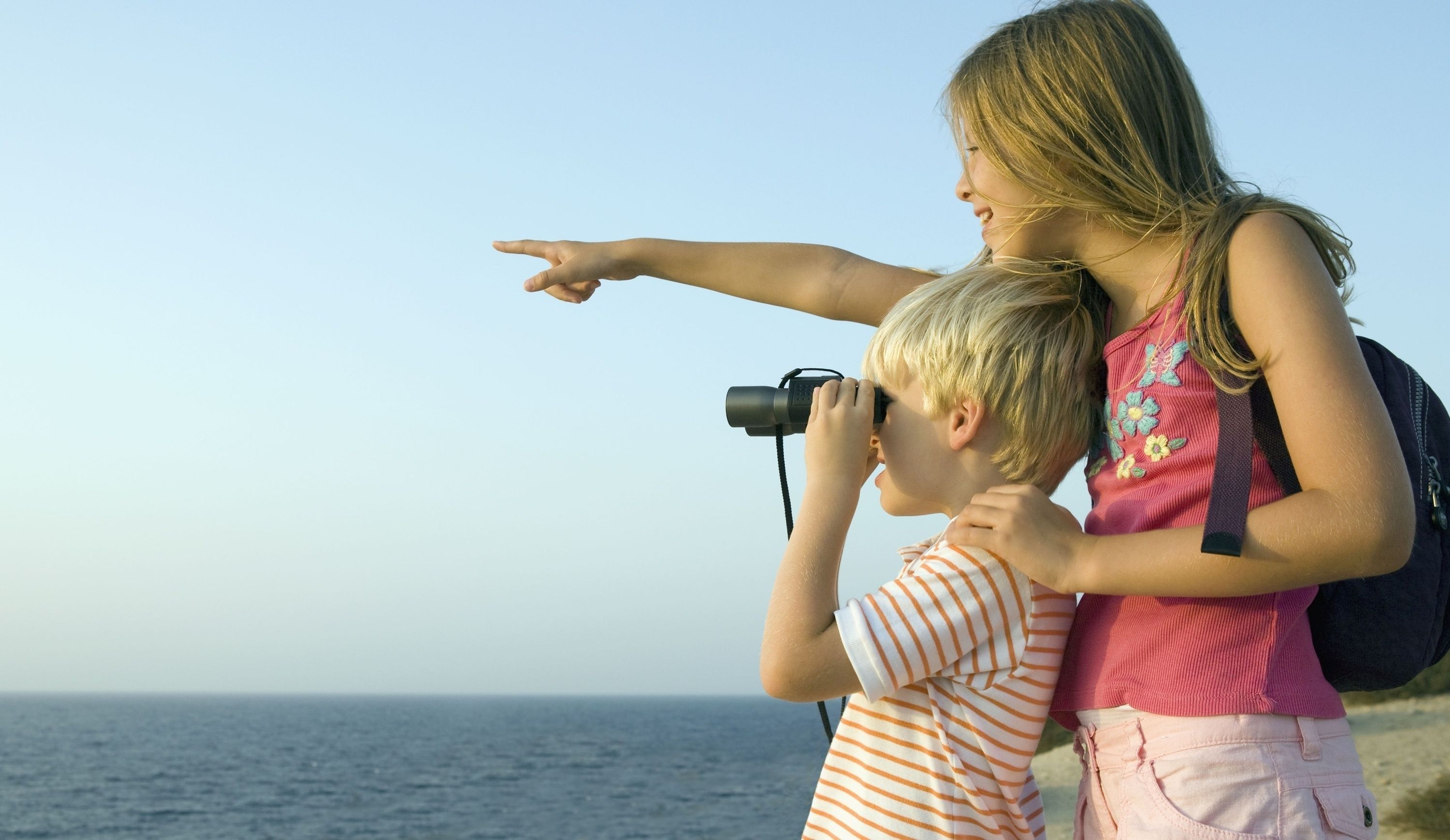 A woman pointing towards the ocean with a child holding a camera.
