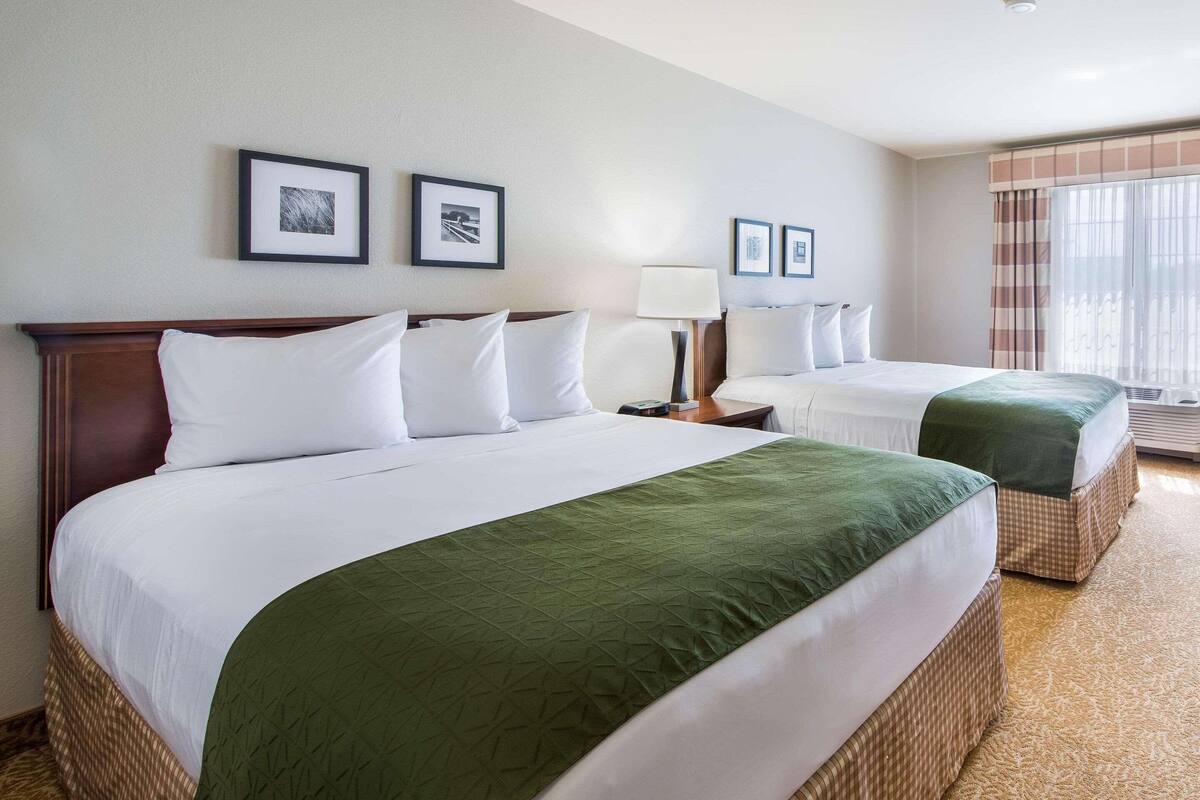 A hotel room with two beds, a large window with curtains, and framed pictures on the wall.