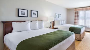 A hotel room with two beds, a large window with curtains, and framed pictures on the wall.