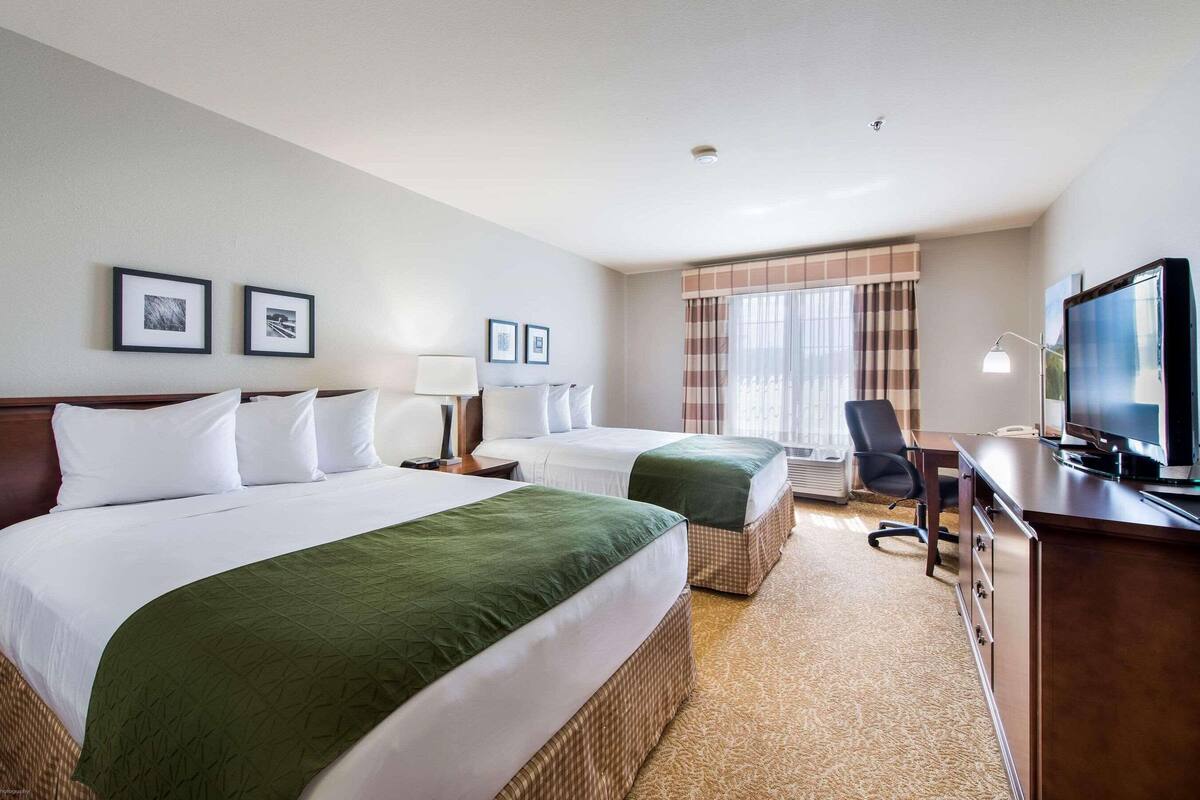 A hotel room with two beds, a desk with a computer, a TV, and a window with curtains.