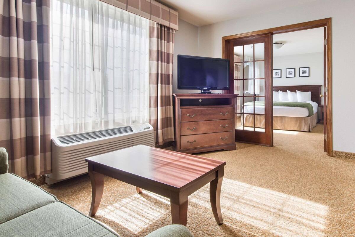 A hotel room with a bed, a television, a desk, and a window with curtains.