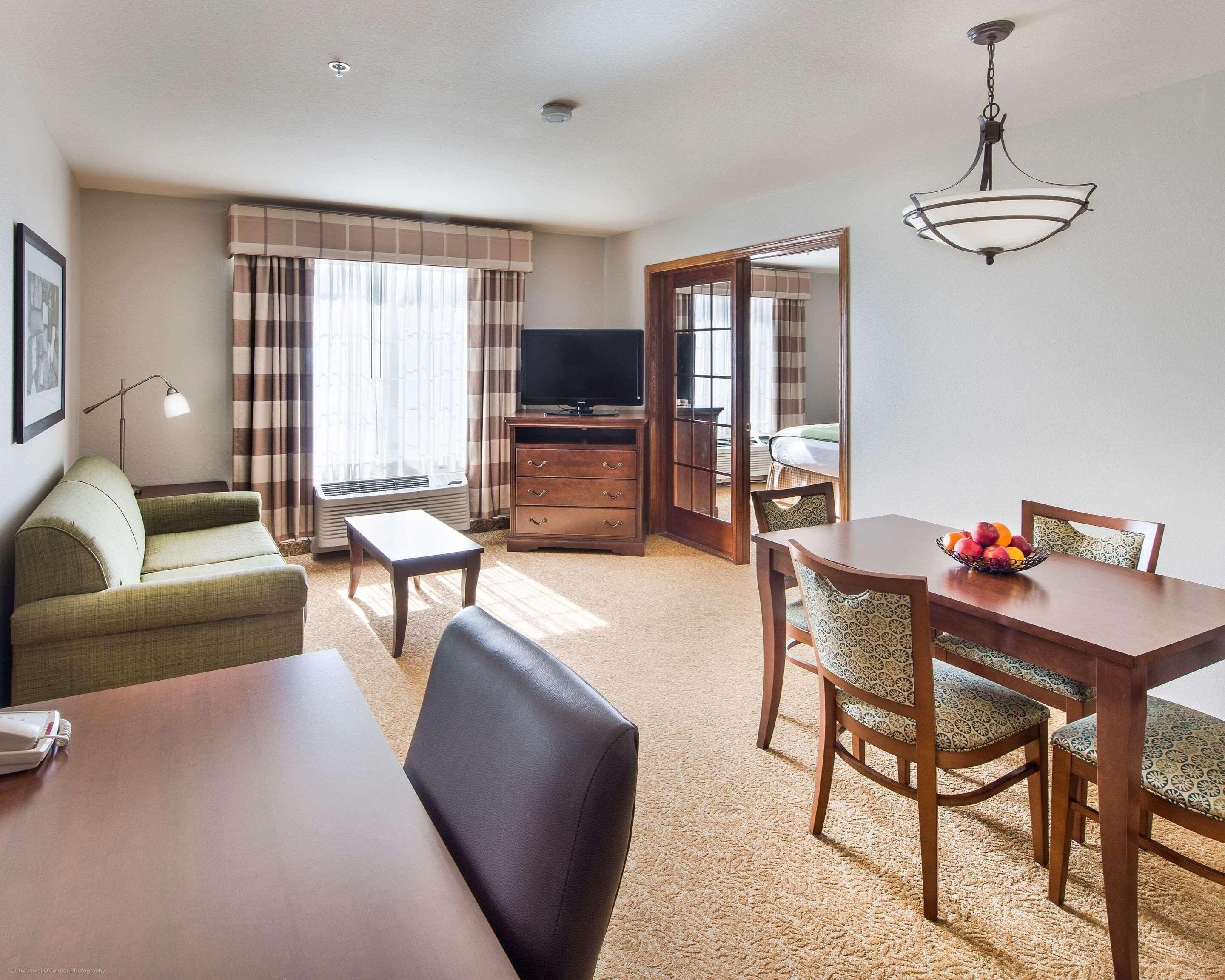Una habitación de hotel con sofá, una mesa de comedor con sillas, televisión y espejo.