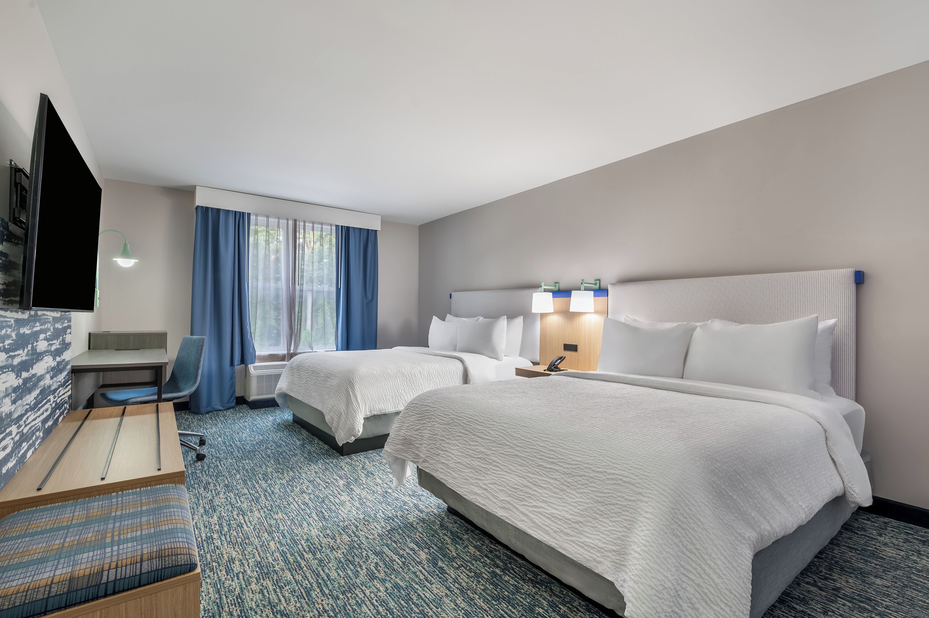A hotel room with two beds, a desk, a chair, and a television.