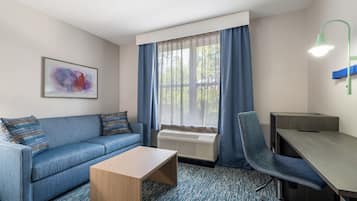 Habitación de hotel con sofá, una mesita, escritorio, silla, radiador, ventana con cortinas y una lámpara de pared.