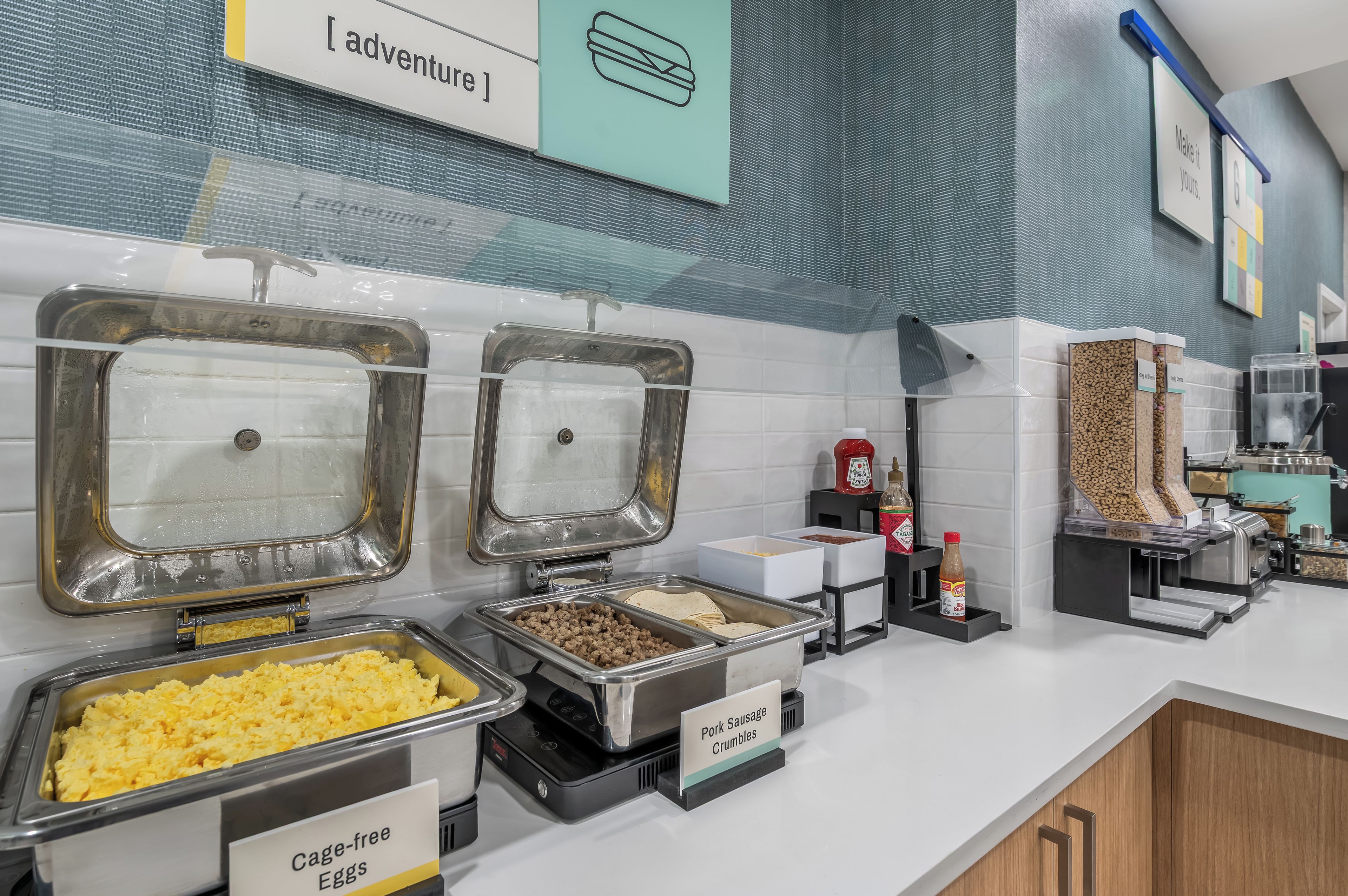 Zona de buffet con opciones de comida identificadas, incluyendo huevos, salchicha y una sección señalizada como 'adventure'.