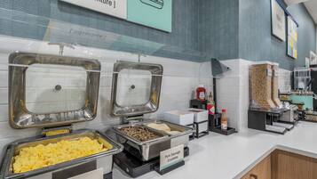 Zona de buffet con opciones de comida identificadas, incluyendo huevos, salchicha y una sección señalizada como 'adventure'.