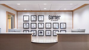 A hotel reception desk with framed portraits on the wall, a sign reading 'Garner AN IHG HOTEL,' and a modern, minimalist design. - Garner Hotel Birch Run Frankenmuth Area by IHG (Birch Run)