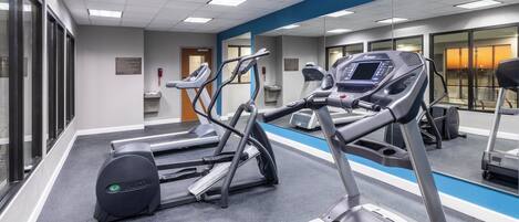 Un gimnasio con cintas de correr, elípticas y un espejo grande.