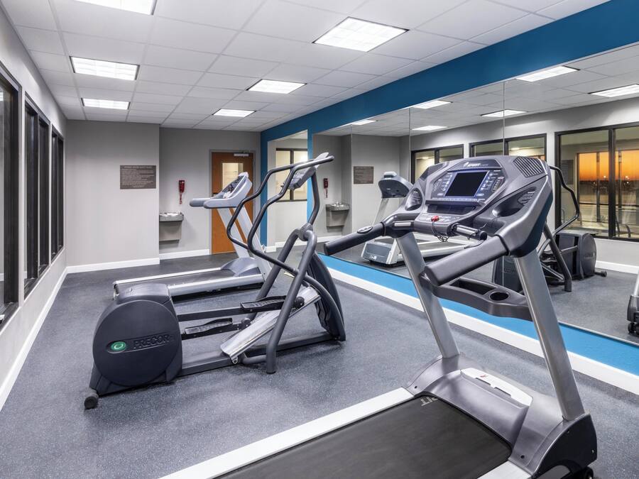 Une salle de sport équipée de tapis de course, de vélos elliptiques et d’un mur recouvert de miroirs.