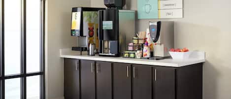 Una estación de café moderna con una máquina de café, un dispensador de agua caliente y una variedad de condimentos.