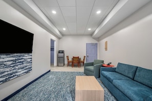 A modern interior with a blue sofa, a wooden coffee table, a dining area with chairs, and a refrigerator.