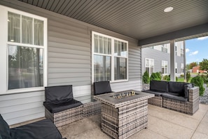 A covered patio area with wicker furniture and a fire feature.