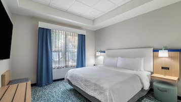 Una habitación de hotel con una cama grande, un escritorio, una silla, un televisor y una ventana con cortinas.