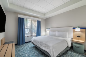 A hotel room with a large bed, a desk, a chair, a TV, and a window with curtains.