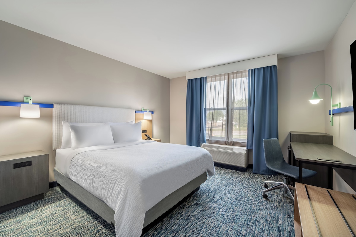 A hotel room with a bed, desk, chair, and a window with curtains.