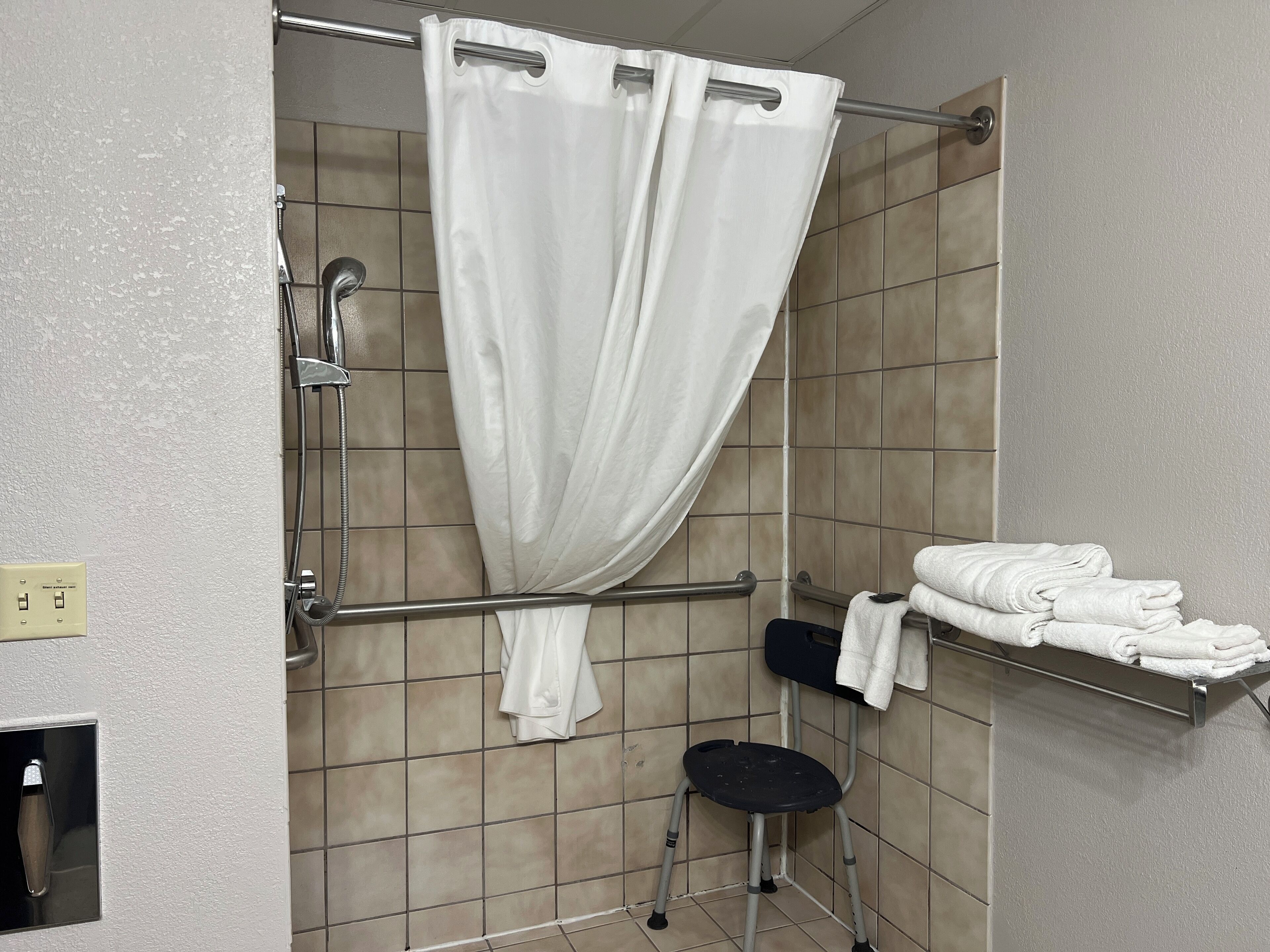 A bathroom with a shower, a grab bar, a towel rack, and a step stool.