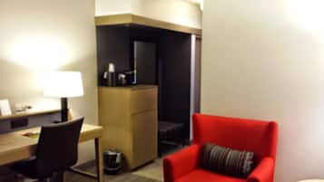 A hotel room with a desk, chair, and a red armchair.