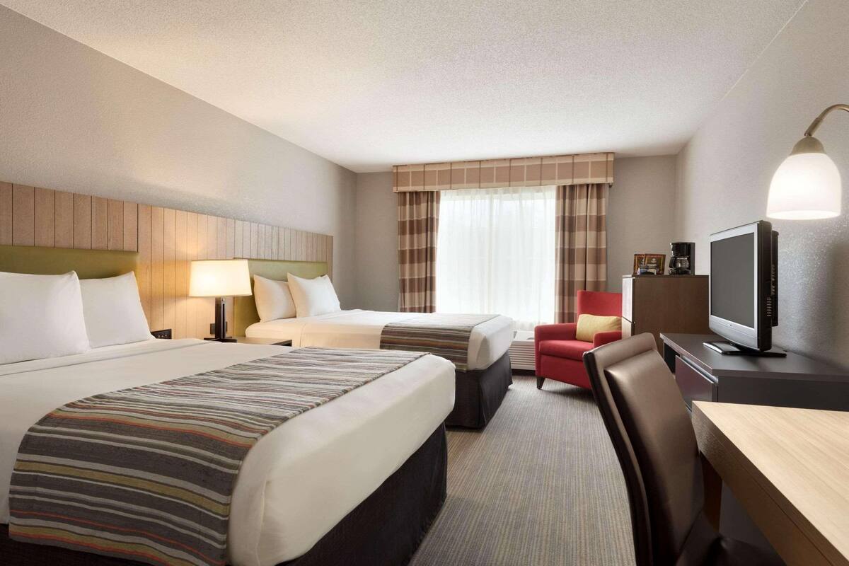 Une chambre d’hôtel avec deux lits, un bureau, une télévision et une chaise.