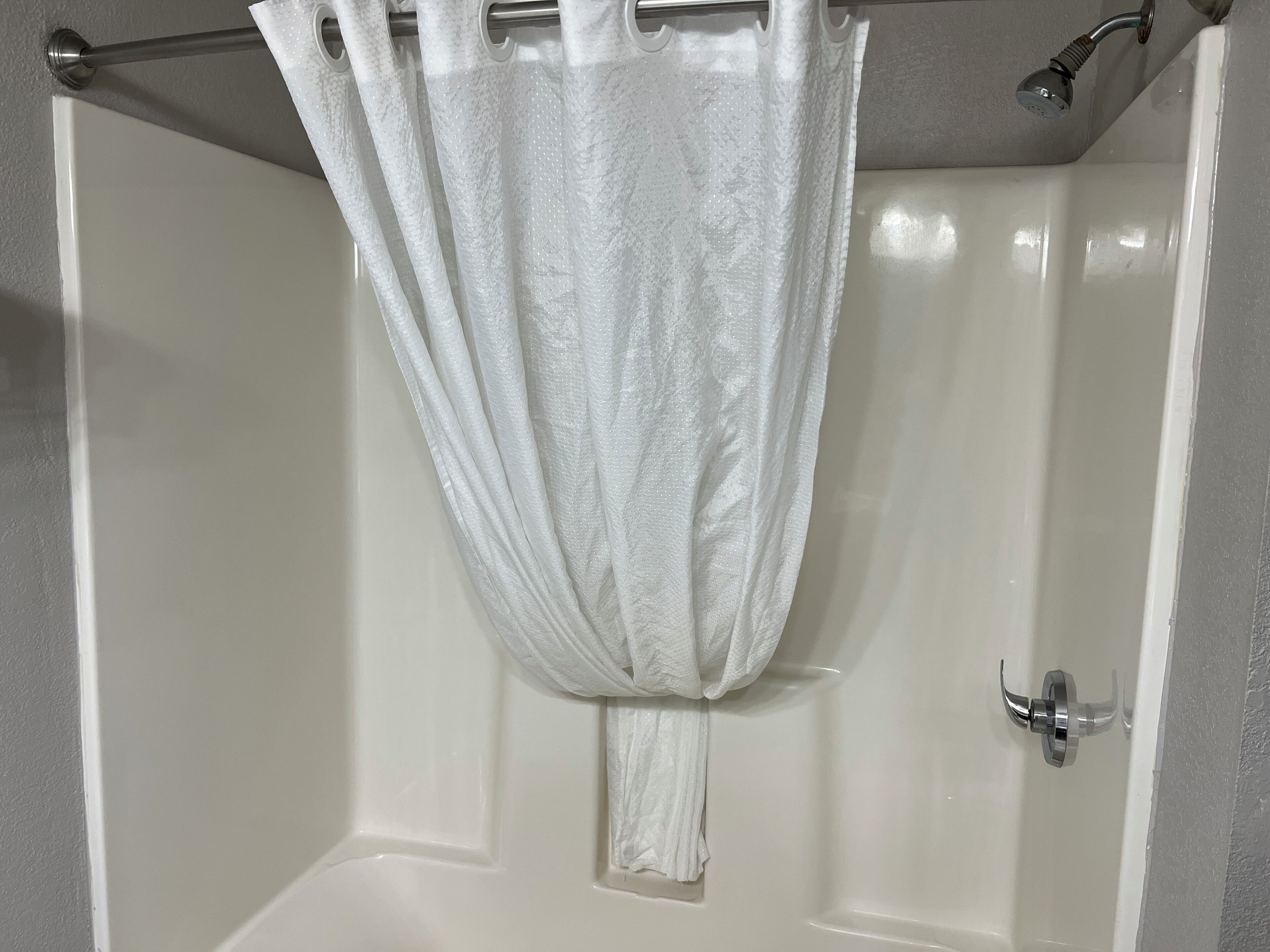 A white shower curtain with a textured pattern, a chrome showerhead, and a white bathtub with a chrome faucet.