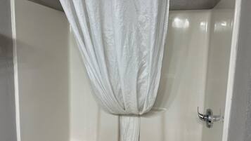 A white shower curtain with a textured pattern, a chrome showerhead, and a white bathtub with a chrome faucet.