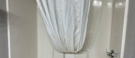 A white shower curtain with a textured pattern, a chrome showerhead, and a white bathtub with a chrome faucet.