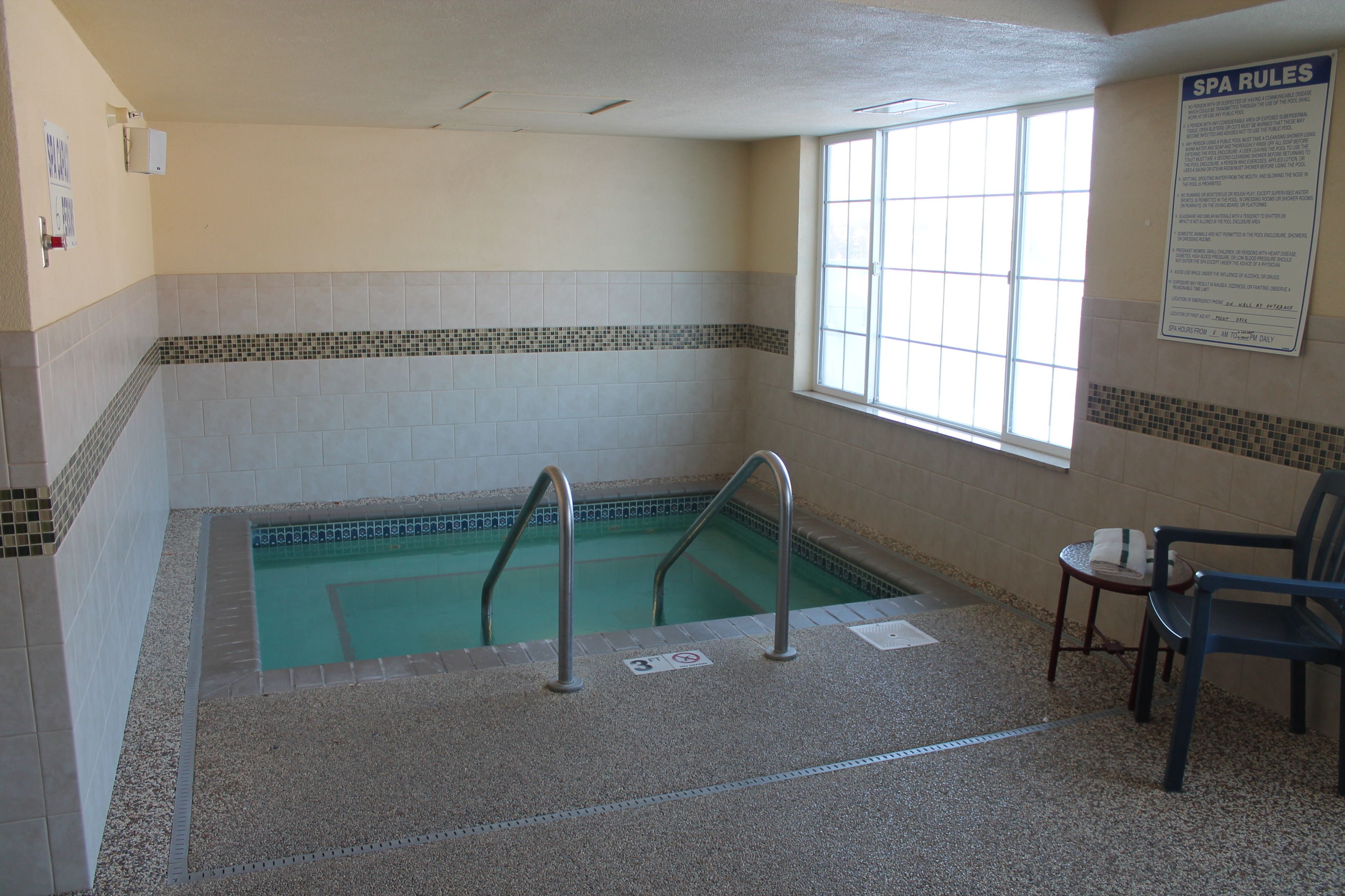 A spa pool area with tiled walls, a window, and a chair.