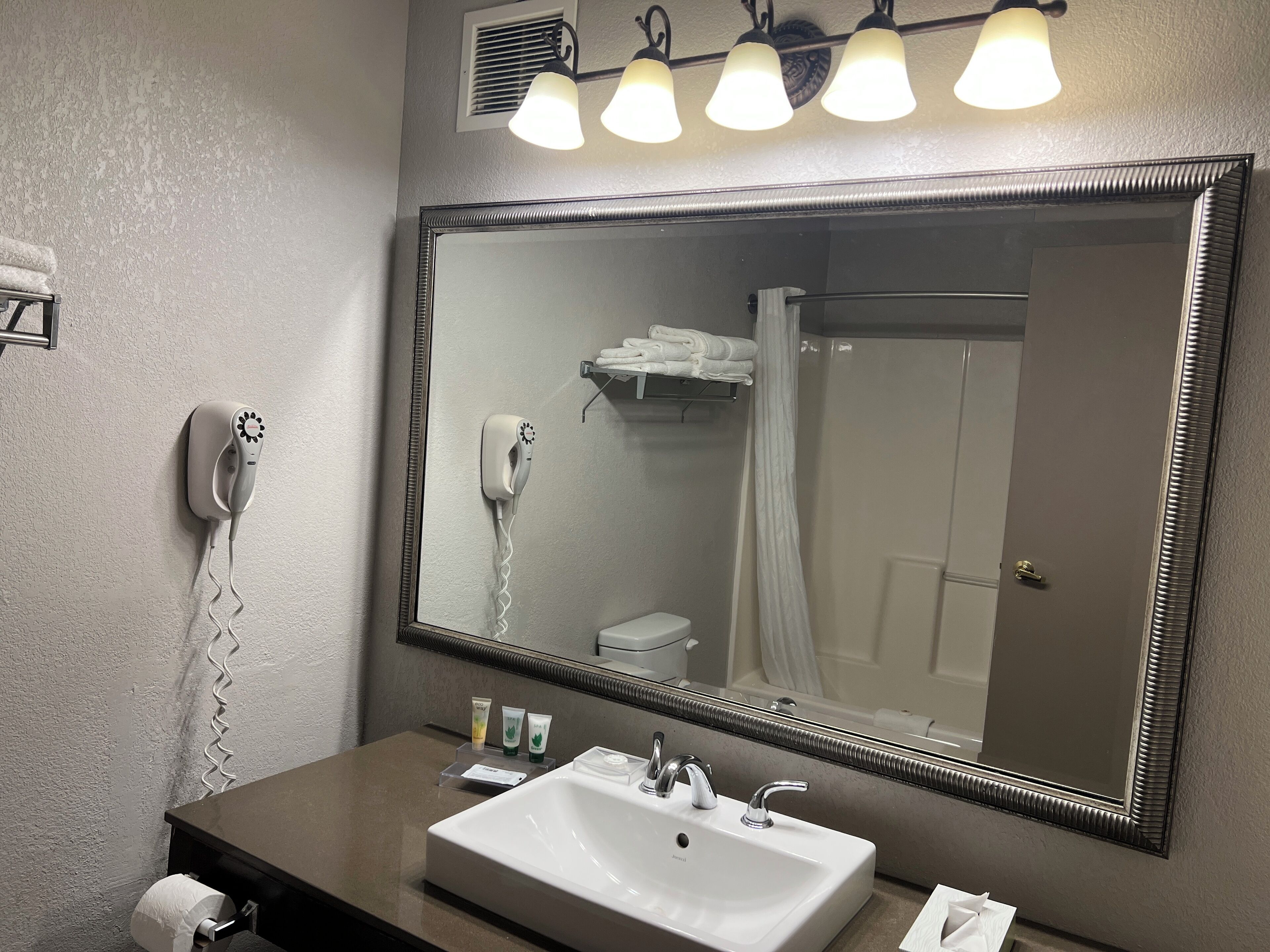 A bathroom with a large mirror, a sink, a hairdryer, and a towel rack.
