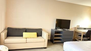Ein Hotelzimmer mit einer Couch, einem Schreibtisch, einem Flachbildfernseher, einem Bett und einem Heizkörper.