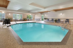 Una piscina interior con agua cristalina, rodeada de sillas y mesas, y amplios ventanales que aportan luz natural.