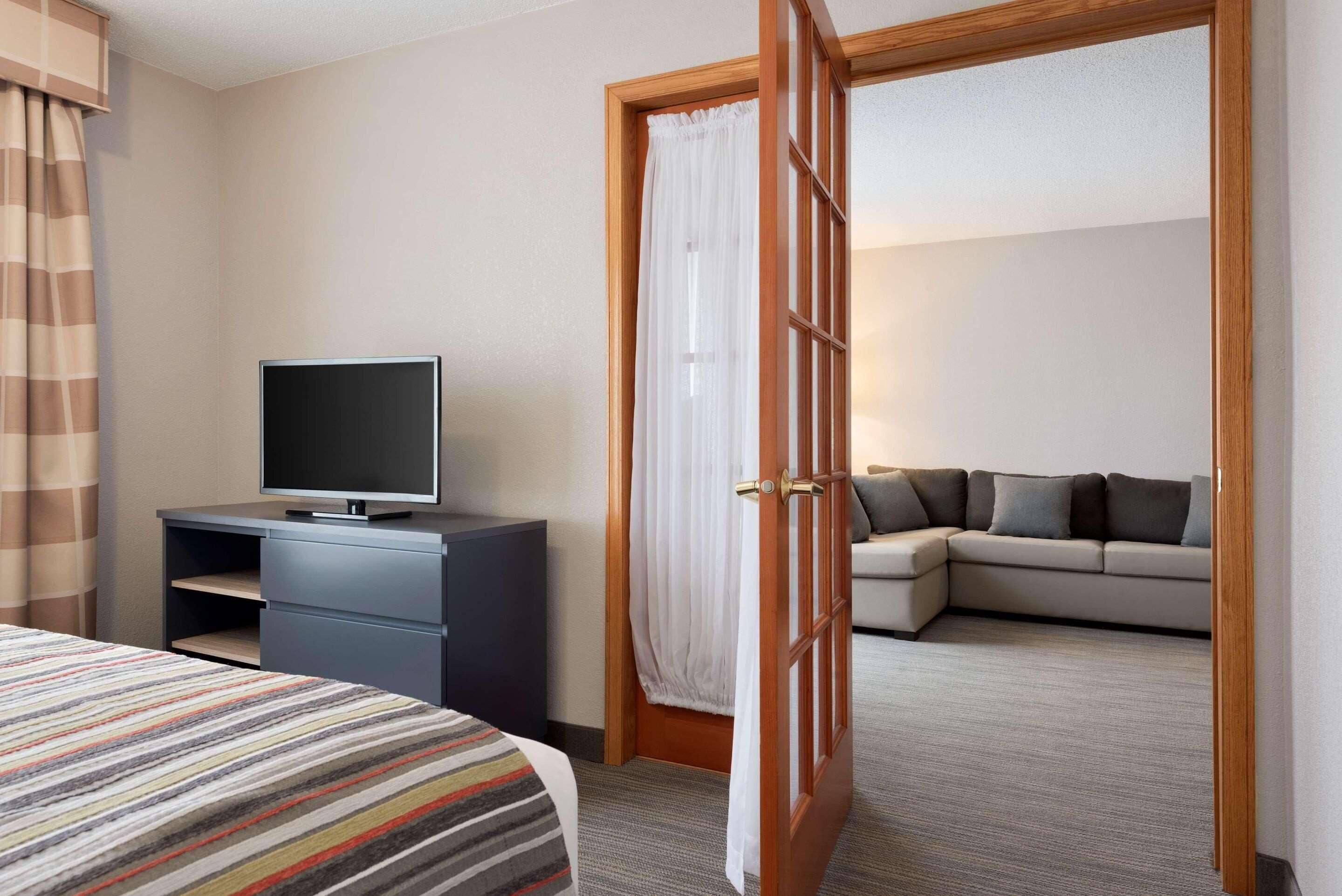 Une chambre d’hôtel avec un lit, un téléviseur posé sur un bureau, un canapé et une porte donnant sur une autre pièce.