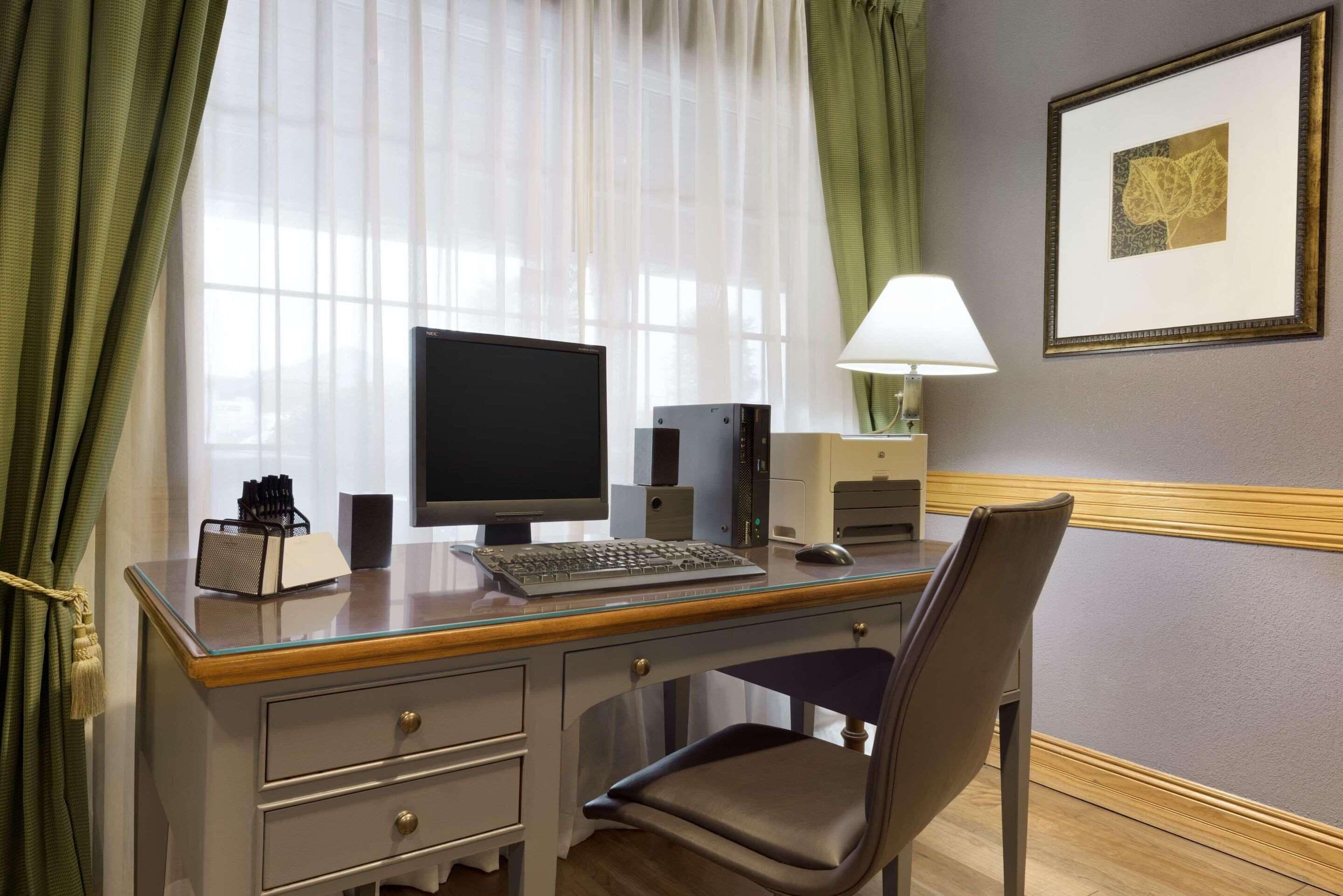 Una habitación de hotel con un escritorio de madera, una computadora, una lámpara y una silla.