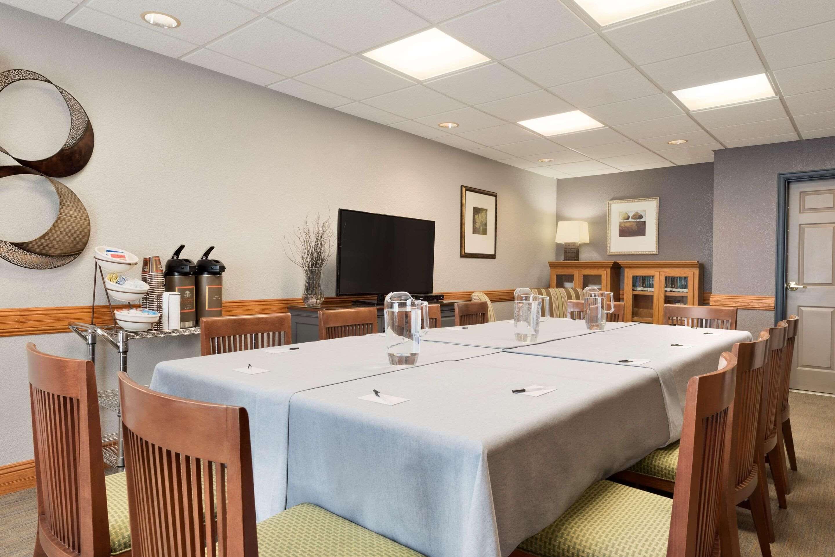 Un salón de conferencias con una larga mesa, sillas, un televisor y un aparador con libros y objetos decorativos.