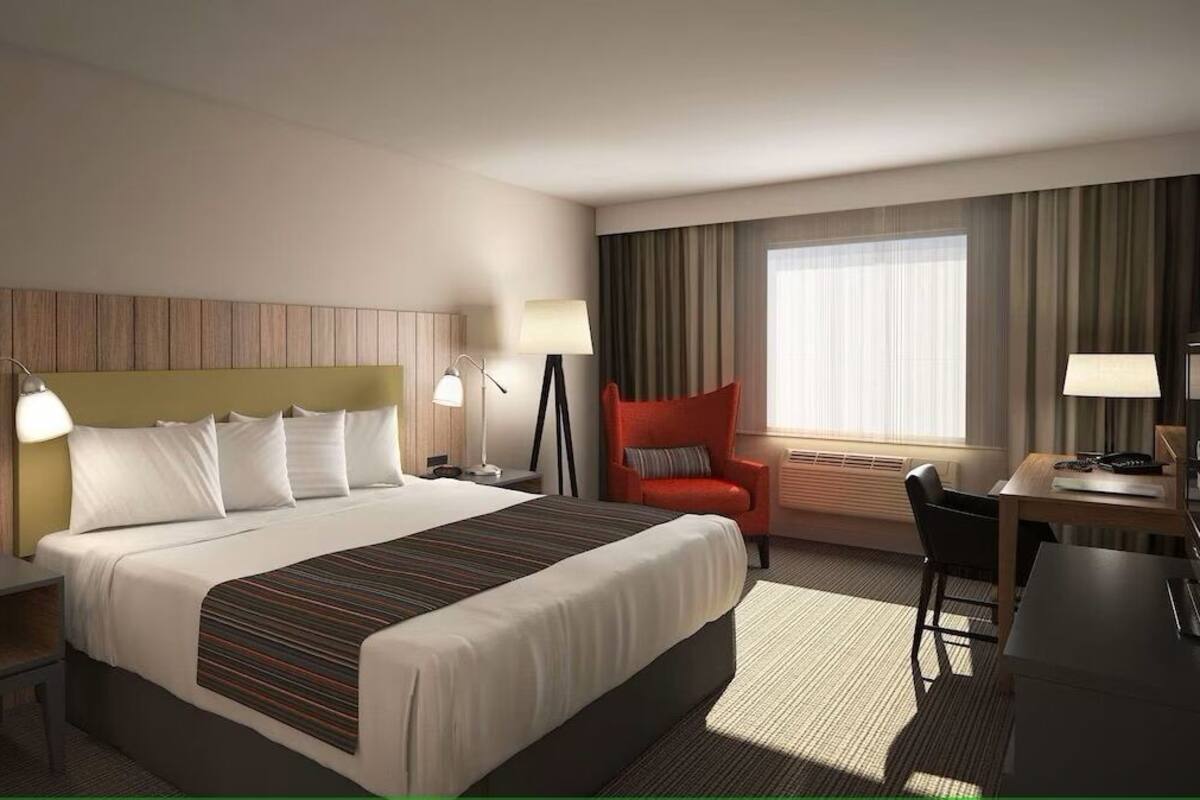Une chambre d’hôtel avec un grand lit, des tables de chevet, un bureau, une chaise et une fenêtre avec des rideaux.
