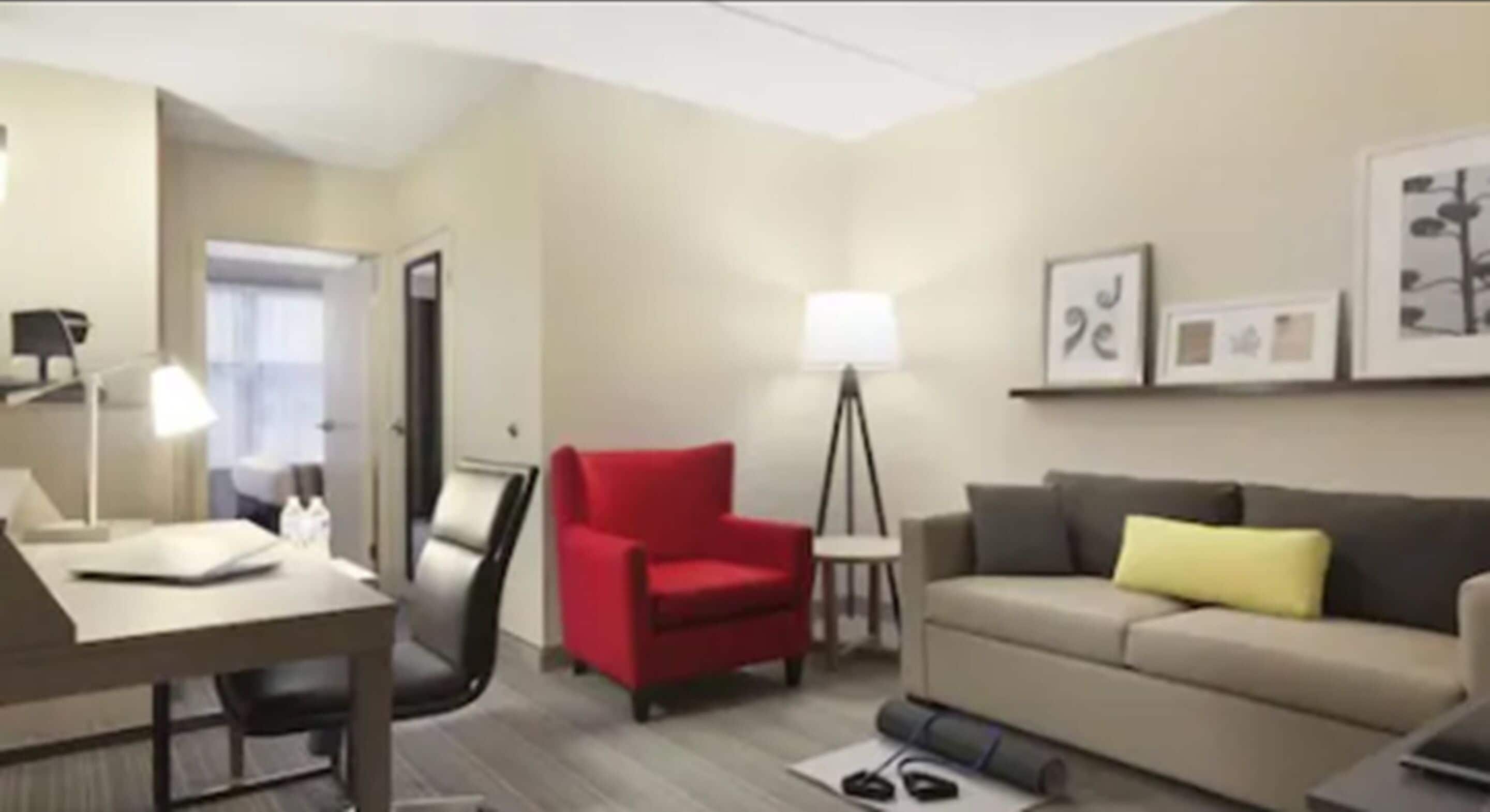 Una habitación de hotel con un escritorio, un sillón rojo, un sofá y una lámpara de pie.