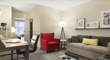 Una habitación de hotel con un escritorio, un sillón rojo, un sofá y una lámpara de pie.