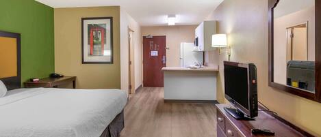 Quarto de hotel com cama, televisão, escrivaninha e cozinha compacta.