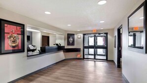 Un espace d’accueil d’hôtel avec un plancher en bois, des œuvres d’art encadrées accrochées aux murs et un panneau indiquant la sortie au-dessus de la porte.