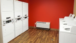 A laundry room with multiple white dryers, a wall-mounted air conditioner, and a wooden floor. - Extended Stay America Suites Dallas Frankford Road (Dallas)