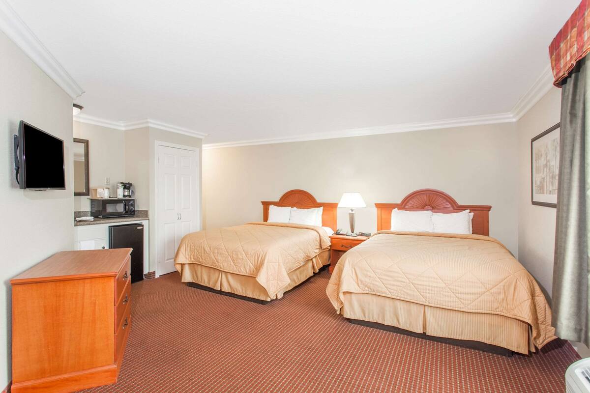 A hotel room with two beds, a TV, a desk with a microwave, and a dresser.
