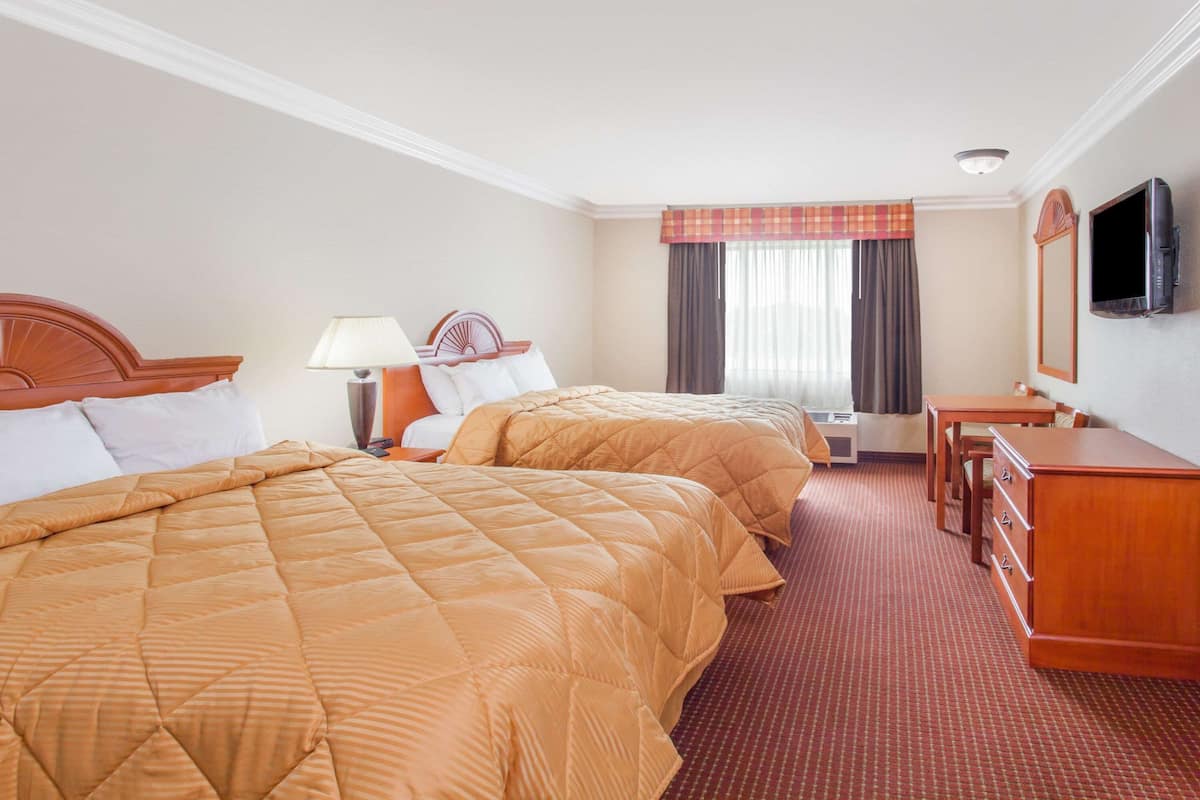 A hotel room with two beds, a desk, a chair, a television, and a window with curtains.