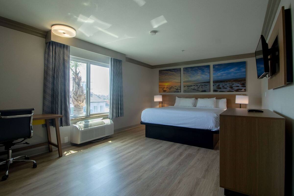 A hotel room with a bed, desk, chair, and a large window.
