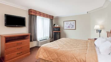 A hotel room with a bed, a TV, a desk, a lamp, and a picture on the wall.