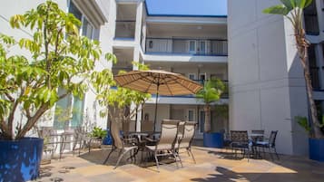 An outdoor patio with a table and chairs, surrounded by potted plants and a large umbrella.
